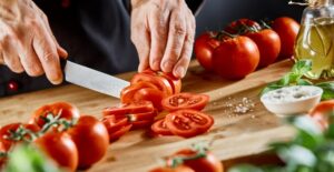 Chef slicing fresh ripe tomatoes on a chopping board