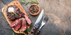 steak-knife-with-herbs-and-a-piece-of-butter-on-the-wooden-tray-view