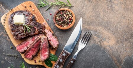 steak-knife-with-herbs-and-a-piece-of-butter-on-the-wooden-tray-view